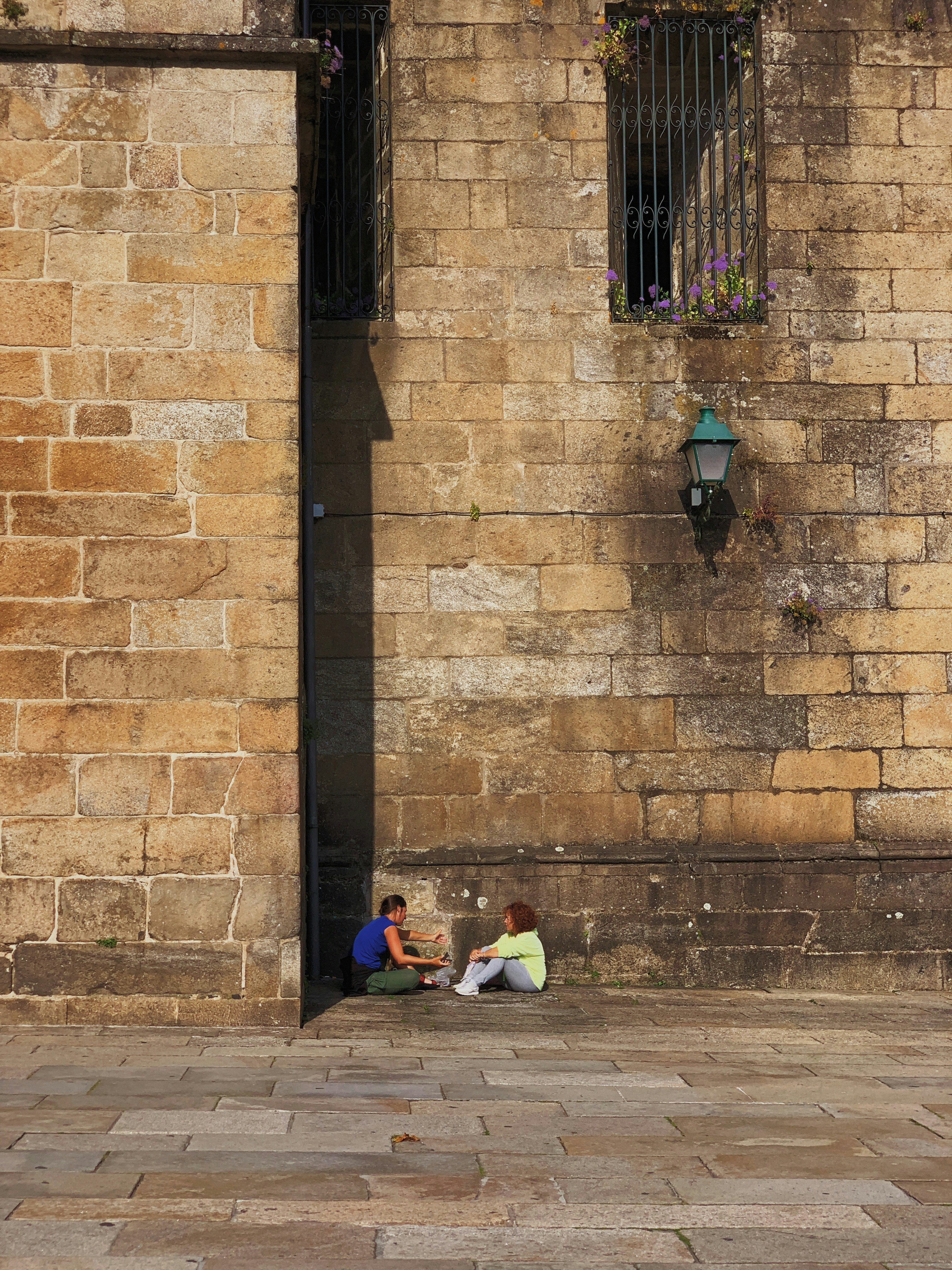 two people sitting at the side of the building